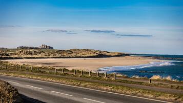 Drive along the scenic coastal road to a picturesque beach with a majestic castle in the distance.