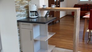 Une cuisine compacte équipée d’une machine à café, d’un petit placard et d’une table en bois avec deux tasses.