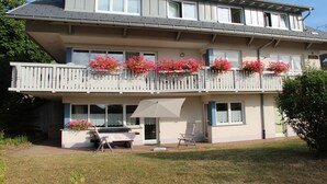 Une maison à deux étages avec un balcon, une terrasse dotée d’une table et de chaises, et une jardinière ornée de fleurs roses.
