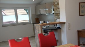 Une cuisine compacte avec une table en bois et des chaises rouges, une fenêtre avec des stores et un four à micro-ondes placé au-dessus du plan de travail.