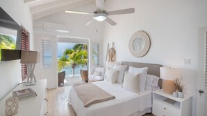 Une chambre à coucher avec un lit, des tables de chevet, un ventilateur de plafond et une vue sur les palmiers et l’océan.