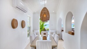 Un espace repas avec une longue table, des murs blancs et une vue sur l’océan.