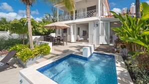 Une maison à deux étages avec une piscine, du mobilier d’extérieur et une végétation luxuriante.