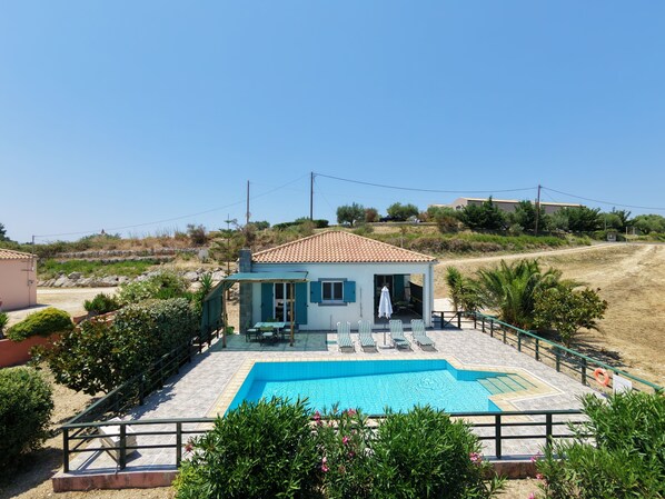 A villa with a swimming pool, outdoor seating, and a view of the surrounding landscape.