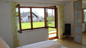 A bedroom with a large window, a bed, a chair, and a wardrobe. - Light-filled, spacious apartment, direct access to terrace and lawn (Ühlingen-Birkendorf)