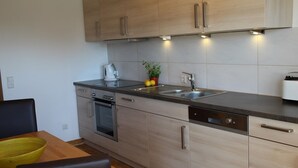 A modern kitchen with light wood cabinets, stainless steel appliances, and a black countertop. - Light-filled, spacious apartment, direct access to terrace and lawn (Ühlingen-Birkendorf)