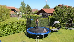 A trampoline in a backyard with a wooden fence, a ladder, and a small table with a chair. - Light-filled, spacious apartment, direct access to terrace and lawn (Ühlingen-Birkendorf)