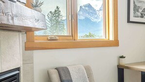 Une pièce chaleureuse avec un fauteuil en bois, une cheminée et une grande fenêtre donnant sur les montagnes.
