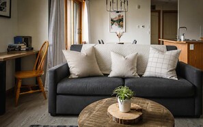 A modern living room with a dark grey sofa, wooden side table, and a round coffee table with a plant.