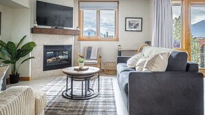 Un salon avec une cheminée, un canapé, un téléviseur et une vue sur les montagnes par la fenêtre.