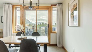 Un coin repas avec une table en bois, des chaises, un lustre et une grande fenêtre agrémentée de rideaux.