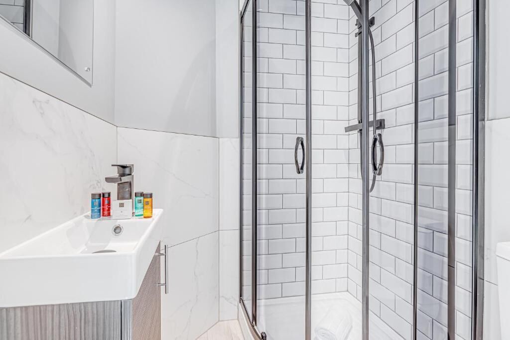Ein modernes Badezimmer mit einem weißen Waschbecken, einer Duschkabine aus Glas und einer Fliesenwand.