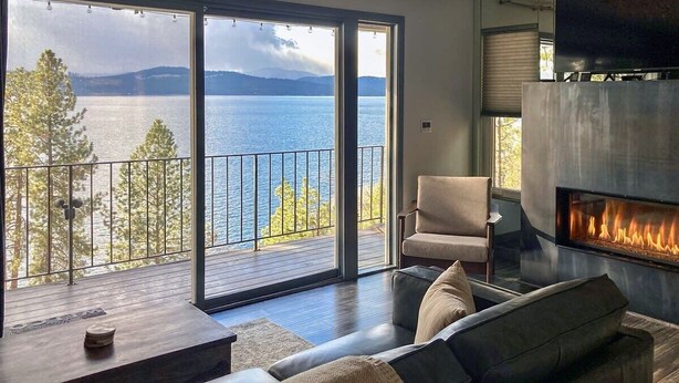 Una sala de estar moderna con un amplio ventanal corredera que da a un balcón con vistas al lago.