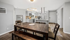 Et moderne køkken med en central ø, et spiseområde med et træbord og bænke, samt en stor hængende lampe over øen.