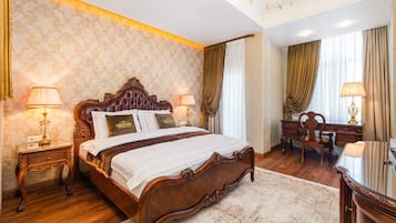 A spacious bedroom with a large bed, two bedside tables with lamps, a wooden desk, and a chair.