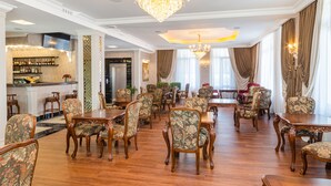 A spacious dining area with wooden tables and chairs, a bar with shelves of bottles, and a chandelier. - GREGORY Boutique Hotel Chisinau (Chisinau)