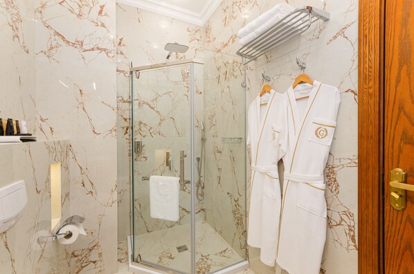 Un baño con ducha de mampara de vidrio, paredes de mármol, un perchero con batas y una puerta de madera.