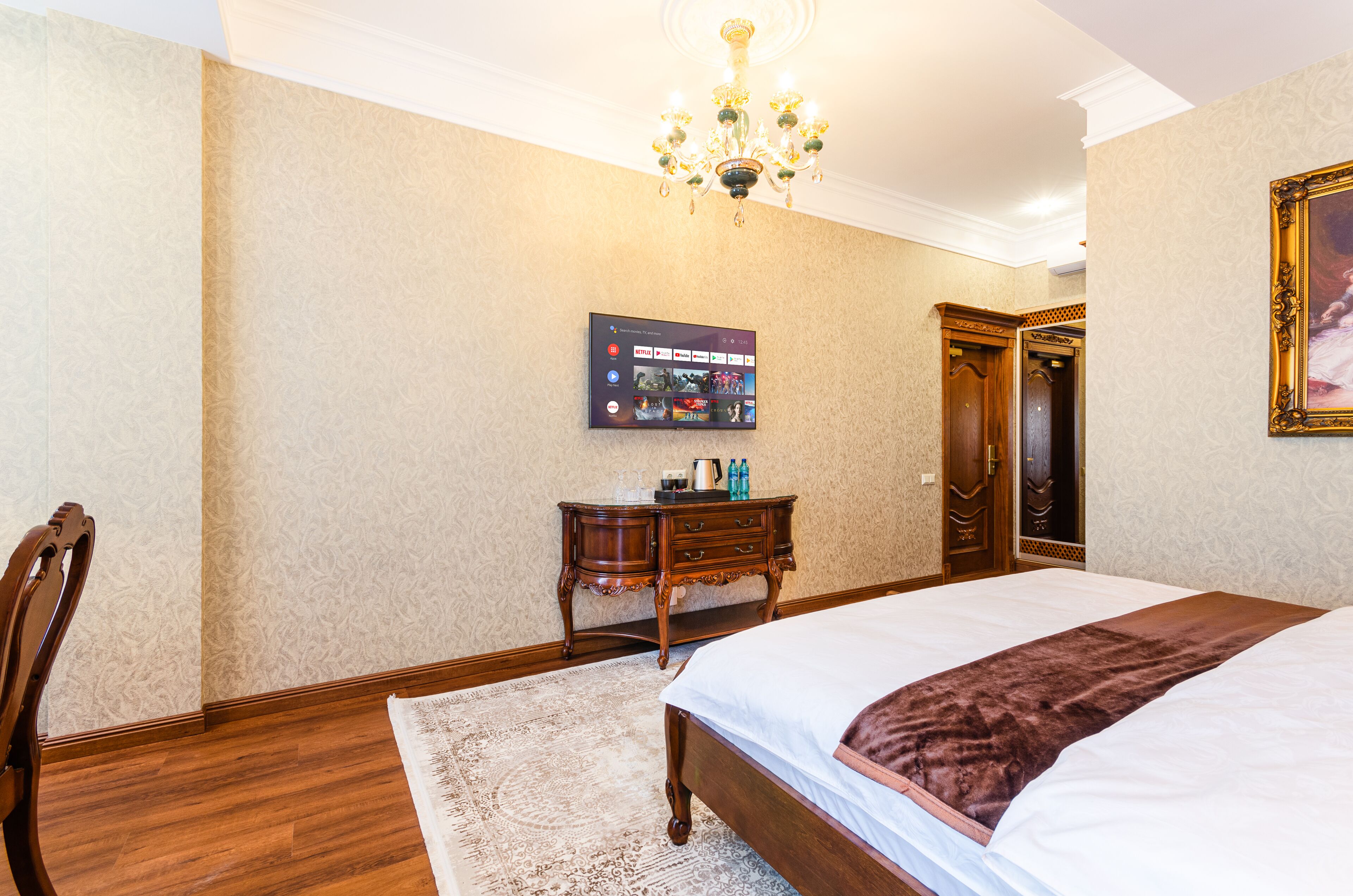 Une chambre d’hôtel avec un grand lit, une commode en bois, un téléviseur à écran plat fixé au mur et un lustre.