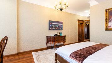 Une chambre d’hôtel avec un grand lit, une commode en bois, un téléviseur à écran plat fixé au mur et un lustre.