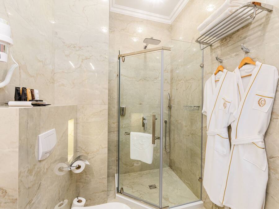 Een moderne badkamer met een douchecabine van glas, marmeren wanden, een handdoekrek met badjassen en toiletartikelen op een plank.
