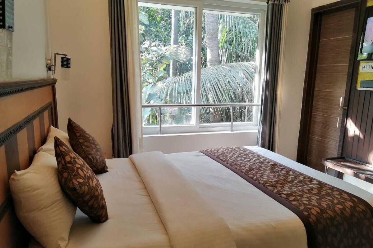 A hotel room with a bed, a window with a view of palm trees, and a door.