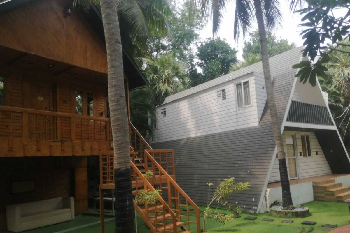 A wooden structure with a balcony, a staircase, and a small garden area with artificial grass and palm trees.