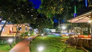 A well-lit outdoor area with a paved walkway, a seating area with cushions, and a pool. -  Leisure Inn Resort by NHospitality (Cheyyur)