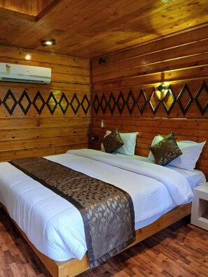 A wooden cabin room with a bed, a nightstand, and a wall-mounted air conditioner. -  Leisure Inn Resort by NHospitality (Cheyyur)