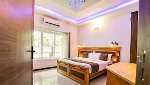 A bedroom with a large bed, a wooden headboard, a nightstand, and a window with curtains. -  Leisure Inn Resort by NHospitality (Cheyyur)