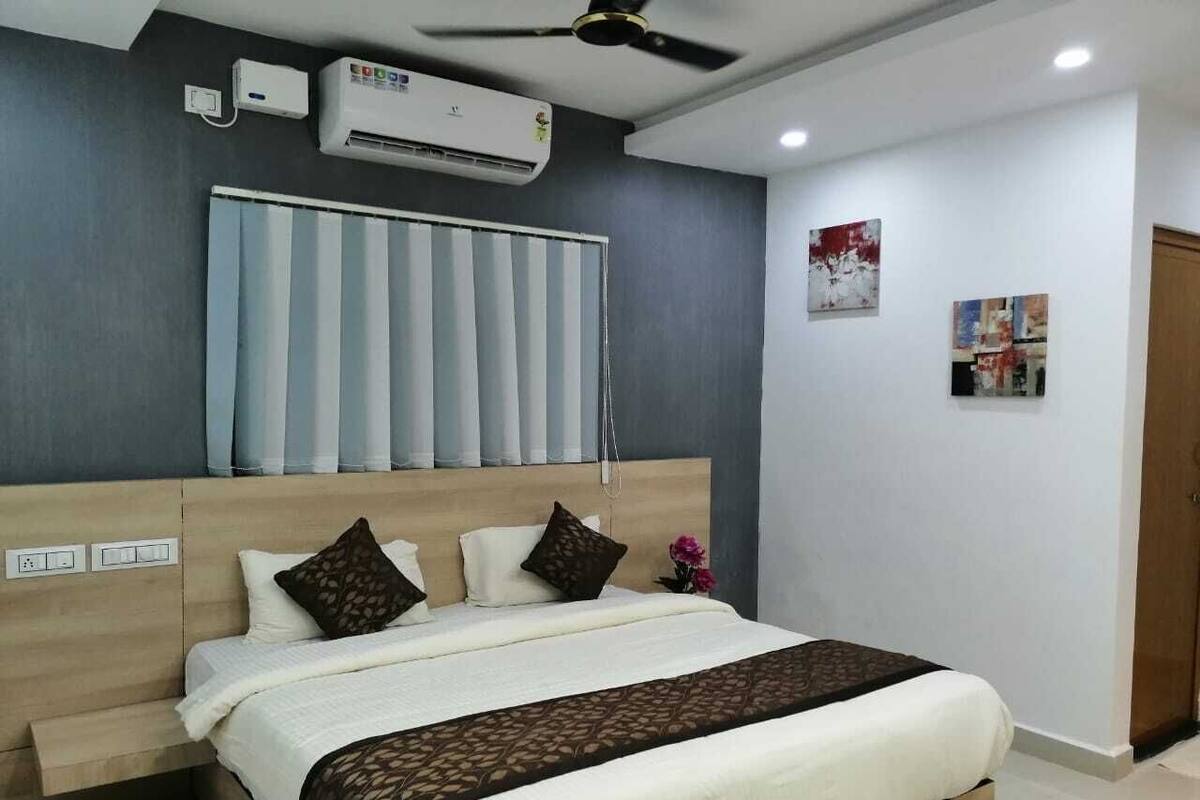 A bedroom with a bed, a ceiling fan, an air conditioning unit, and a window with blinds.