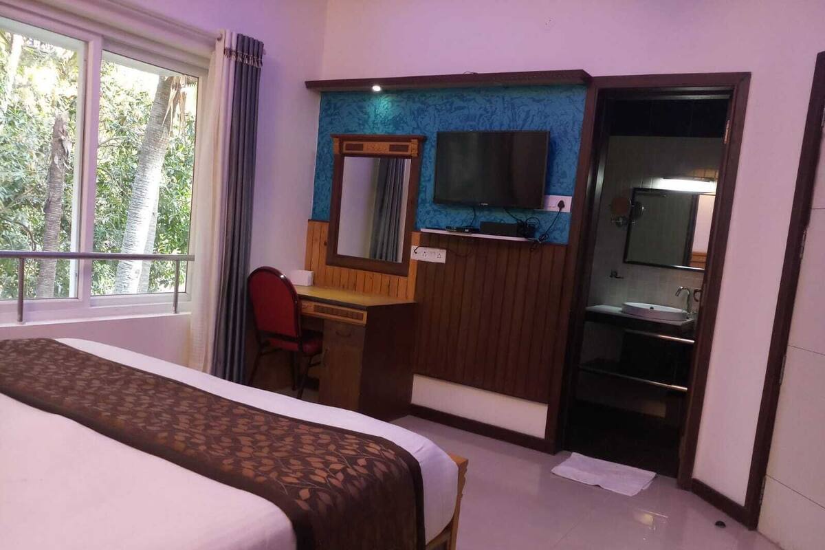 A hotel room with a bed, a desk with a mirror, a television, and a bathroom.