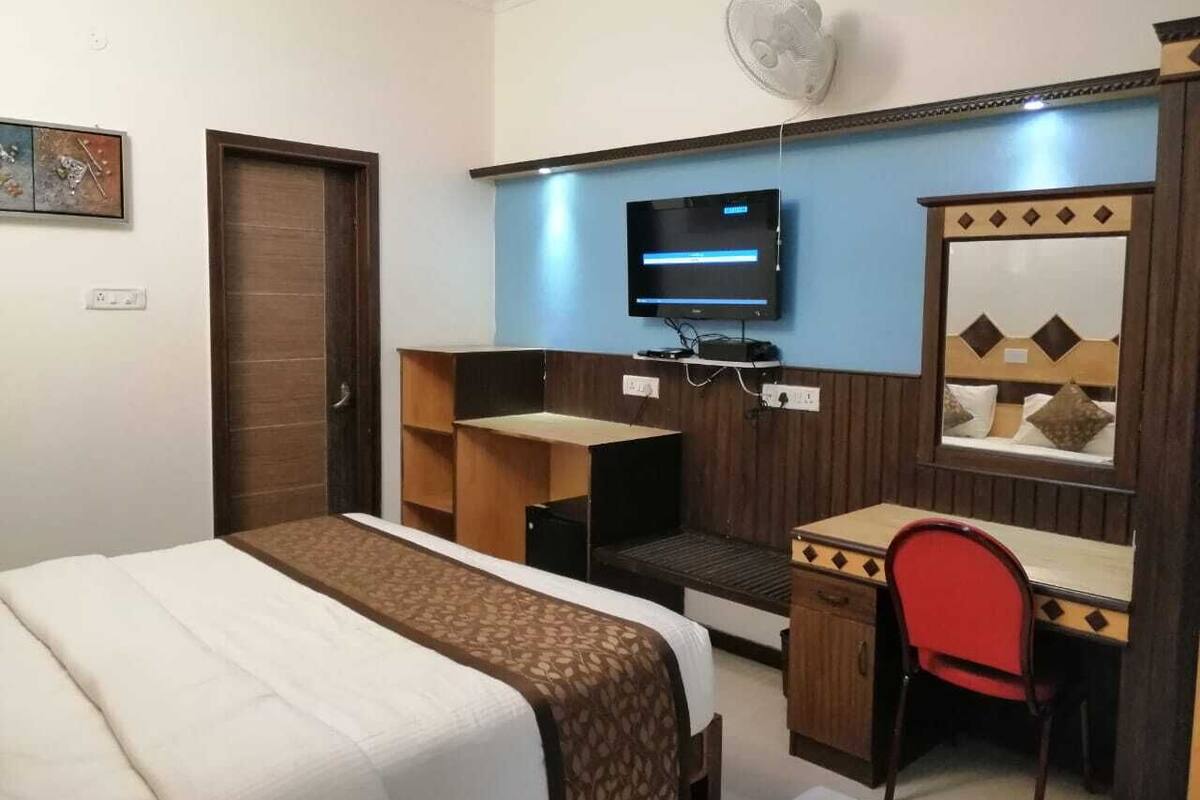 A hotel room with a bed, a desk, a chair, a television, and a mirror.