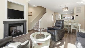 Un salon avec une cheminée, un téléviseur, un escalier et un coin repas.