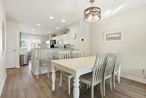 Uma área de refeições com uma mesa e cadeiras brancas, uma cozinha ao fundo e um lustre no teto.