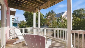 Une véranda couverte avec des balustrades blanches et un seul fauteuil Adirondack.