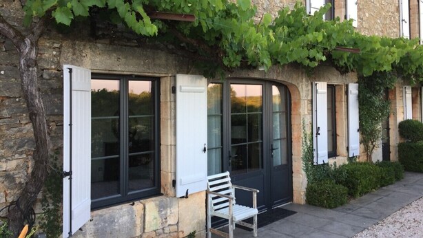 Un bâtiment en pierre doté de grandes fenêtres, d’un banc à l’extérieur et de plantes grimpantes qui recouvrent le mur.