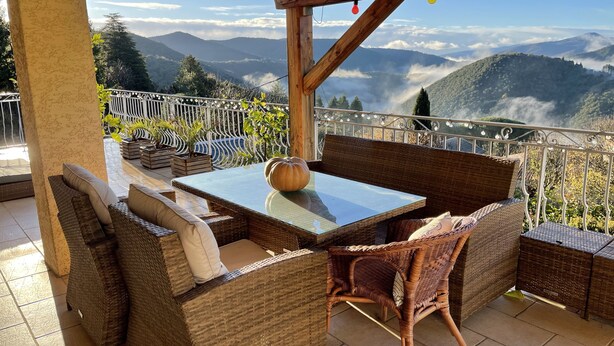 A terrace with wicker furniture, a glass table, and a view of mountains.