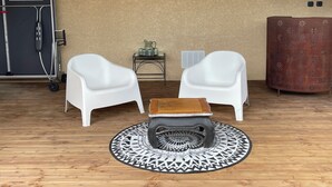 A room with two white armchairs, a small wooden table, a patterned rug, a metal cabinet, and a decorative metal cylinder.