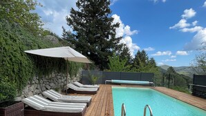 A wooden deck with a pool, lounge chairs, and a stone wall.
