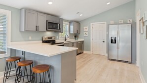 Una cocina moderna con una isla grande, taburetes de bar, electrodomésticos de acero inoxidable y suelo de madera clara.