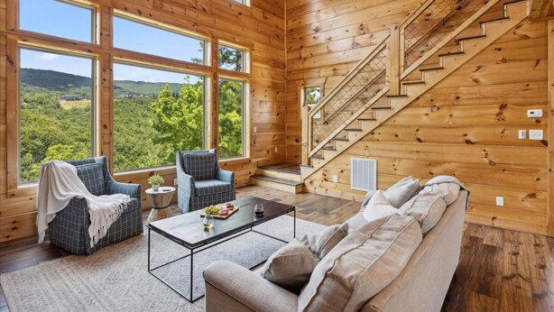 L’intérieur d’un chalet en bois, avec de grandes fenêtres, un escalier, un canapé, une table basse et un fauteuil.