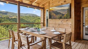 Une terrasse en bois avec une table dressée pour le repas, donnant sur une vallée boisée.