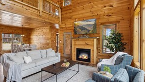 L’intérieur d’un chalet confortable en bois, avec une cheminée, un canapé, une table basse et un téléviseur fixé au-dessus de la cheminée.