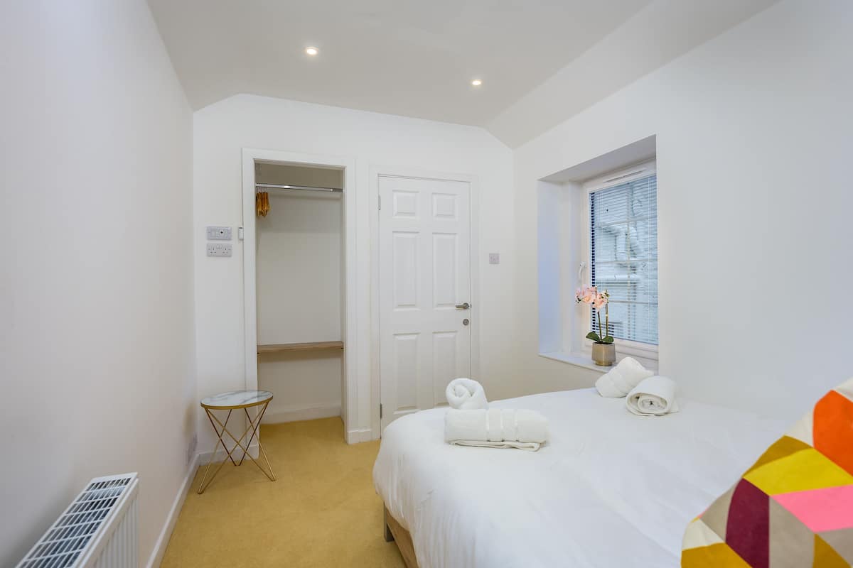 A bedroom with a bed, a window with blinds, a radiator, and a small table.