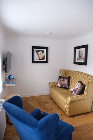 Un salon avec un canapé, un fauteuil bleu, un téléviseur et deux tableaux encadrés accrochés au mur.