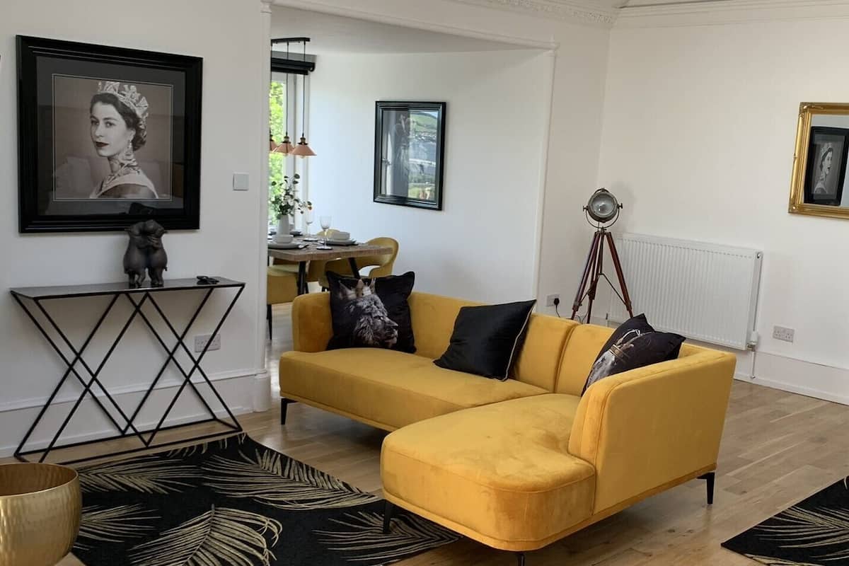 A living room with a yellow sofa, a black and white patterned rug, and a framed picture on the wall.