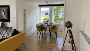 A dining area with a table set for four, a yellow sofa, and a tripod in the corner. - The Clarendon (Dundee)