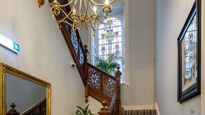 A staircase with a wooden railing and striped carpet, a radiator, a mirror, and a chandelier. - The Clarendon (Dundee)