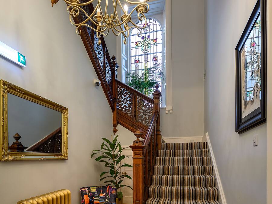 A staircase with a wooden railing and striped carpet, a radiator, a mirror, and a chandelier.