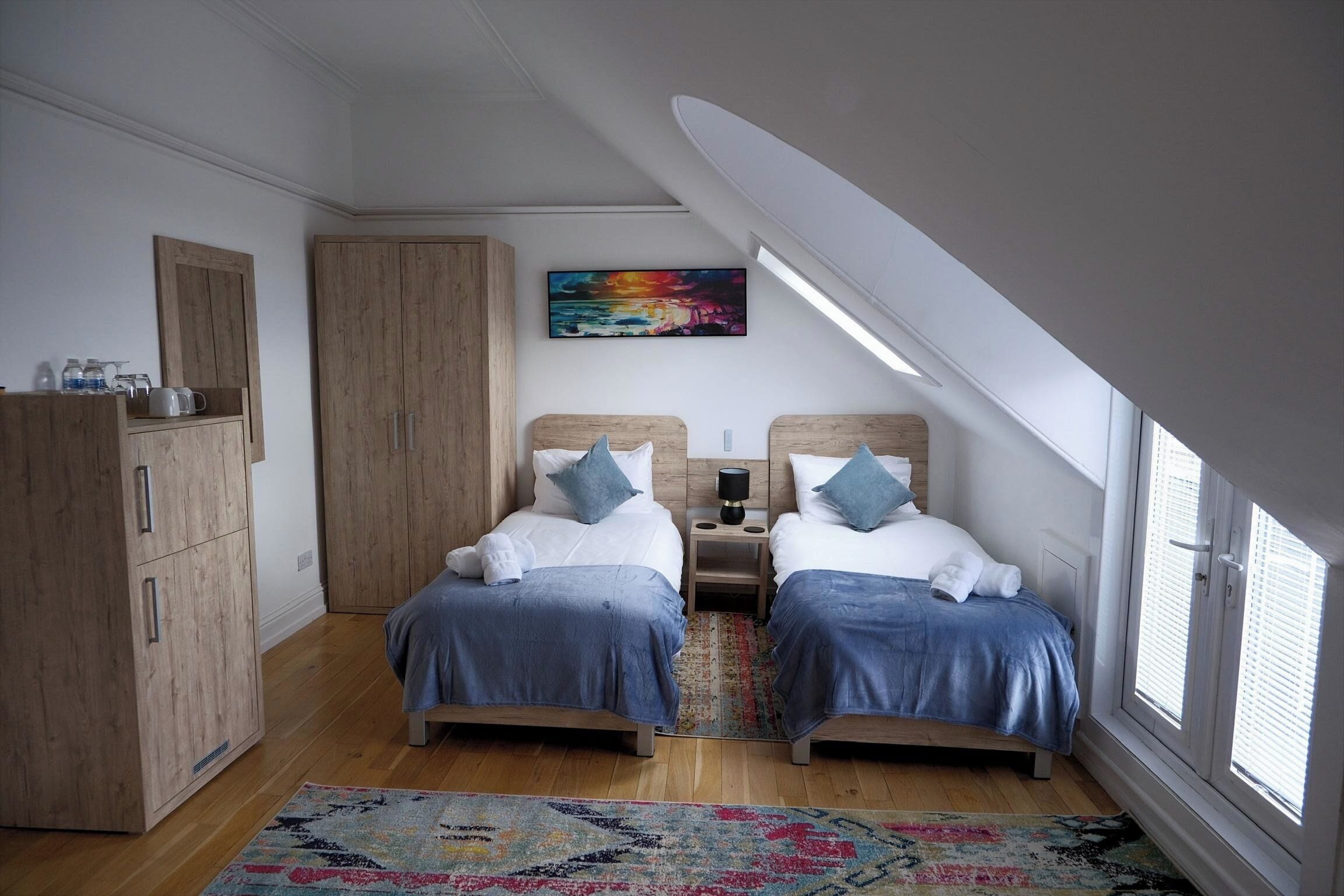 Un dormitorio con dos camas, un armario de madera, una alfombra colorida y un cuadro en la pared.